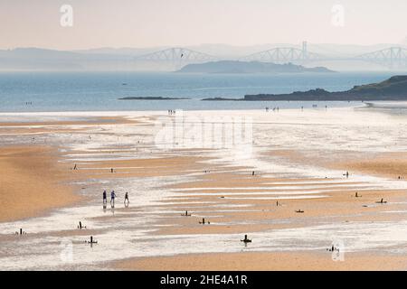 figures on Pettycur Beach, Pettycur Bay, Kinghorn, Fife, Scotland, UK at low tide with Forth Road and rail bridges in the distance Stock Photo