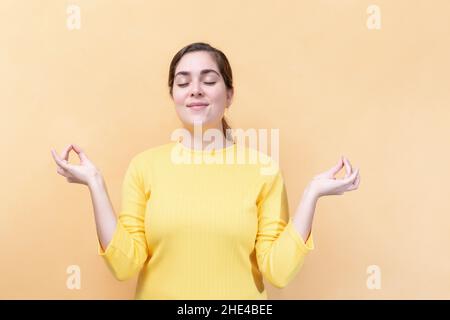 Hold hands in yoga gesture relaxing meditating keeping eyes closed. Young girl on light orange background. Body language. Stock Photo