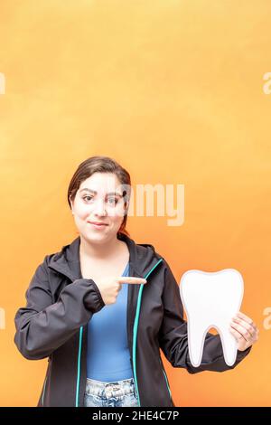 Girl pointing to a tooth shape, isolated over orange background. Stock Photo