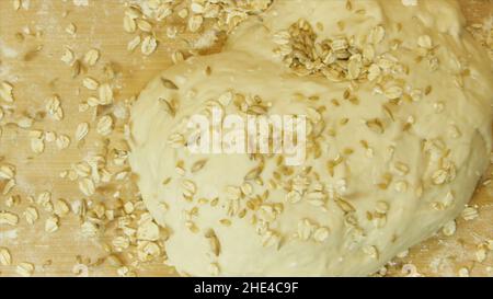 A homemade bread dough with grains and seeds. Top view of many flakes and seeds falling down on raw dough isolated on black background, cooking concep Stock Photo