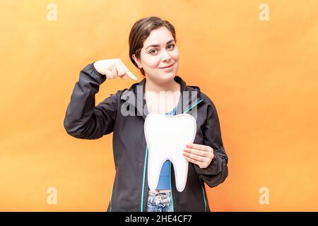 Girl pointing to a tooth shape, isolated over orange background. Stock Photo