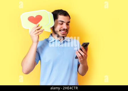 Young man holds up a speech balloon with a heart and used the smart phone. Social media concept. Stock Photo