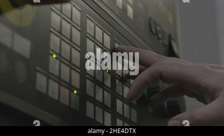 Close up of a hand presses buttons on the control panel of industrial equipment. Side view of male hand pushing the button at the factory panel. Stock Photo