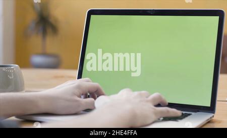 A man is working at home and using laptop with green screen, communication and business concept. Man typing on his computer with chroma key. Stock Photo