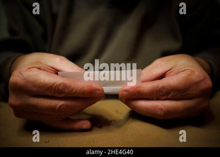 A man rolls a cigarette paper and fills it with loose tobacco Stock Photo