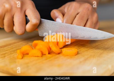 Detailed shot of a male cutting carrot on a wooden cutting board. Stock Photo