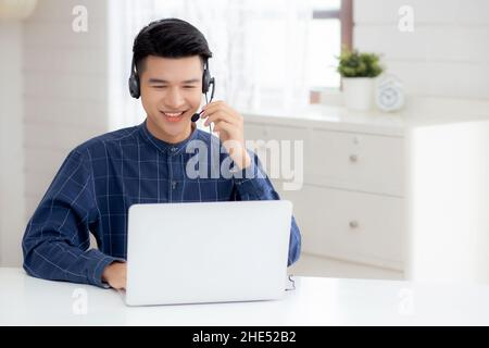 Young asian businessman working on laptop computer wearing headphone at home, business man wearing headset for video conference, communication and edu Stock Photo