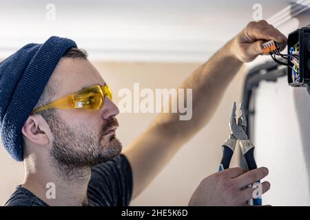 An electrician is mounting electric sockets on the white wall indoors. Stock Photo