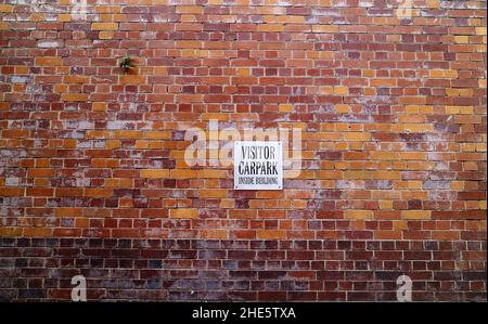 Metallic visitor carpark sign on heritage listed old multicoloured brick wall in Brisbane Australia Stock Photo