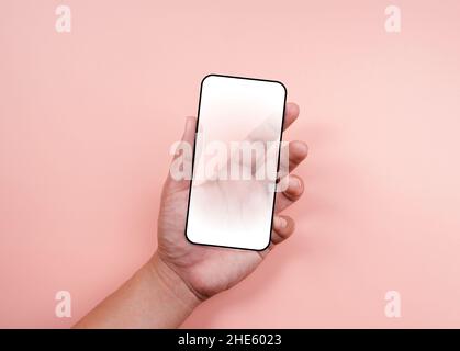 Hand holding smartphone with a white blank screen with black frame isolated on pastel pink background. Mockup transparent future phone in hand, minima Stock Photo