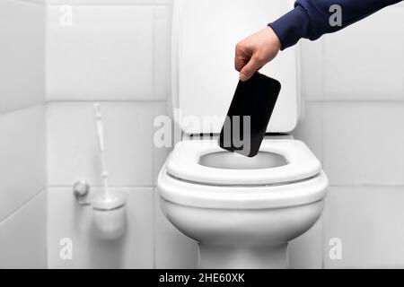 a man throws a mobile phone smartphone into the toilet with his hand. liberation from social dependence and fatigue from communication. the desire to Stock Photo
