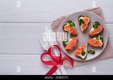 Mini sandwiches with salmon, curd cheese, parsley and rye bread in form of hearts. Valentine's day homemade creative food. Love breakfast design. Sele Stock Photo