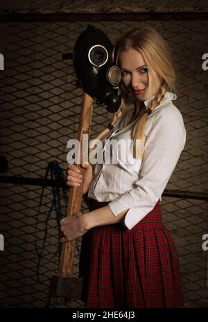 Caucasian Woman wearing casual clothing and toxic protective mask holding axe in an underground warehouse Stock Photo