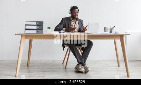 Young black businessman making video call, using laptop at office, having web conference with clients against white wall Stock Photo