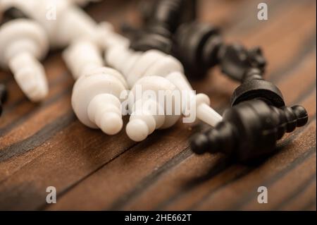 Black and white chess pieces scattered on a wooden table, close-up, selective focus Stock Photo