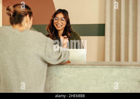 Smiling receptionist assisting a woman with signing in to an office. Friendly receptionist showing a woman where to sign on a clipboard. Young woman w Stock Photo