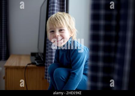 Toddler child, sitting on the window, watching the snow falling, reading little book Stock Photo
