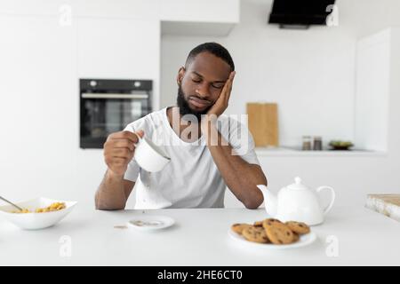 Black man yawning, pouring coffee away from cup Stock Photo