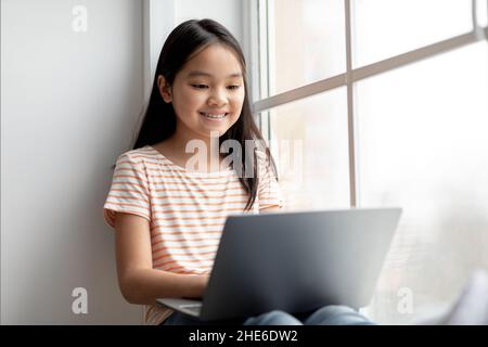 Closeup of cheerful asian kid surfing on Internet, using laptop Stock Photo
