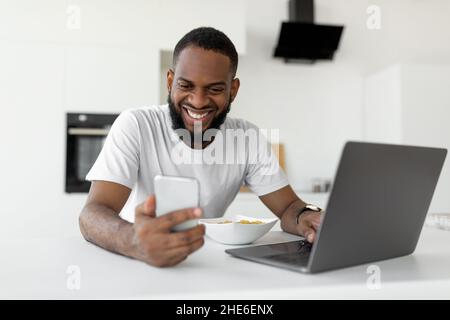 Black man using pc and smartphone having breakfast at home Stock Photo