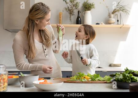 Happy mom giving lettuce leaf to cheerful funny daughter kid Stock Photo