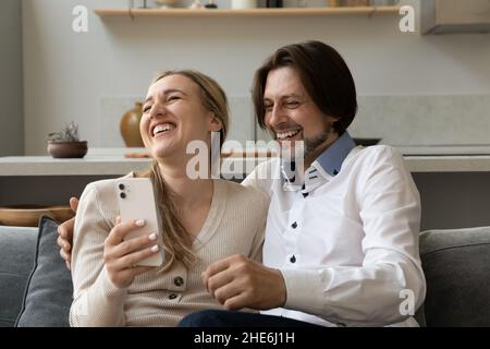 Cheerful excited 40s couple using mobile phone at home Stock Photo