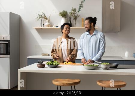 Happy millennial dating African couple preparing salad for dinner Stock Photo