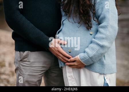 Beautiful shot of a man holding a belly of pregnant woman in blue sweater in a park Stock Photo