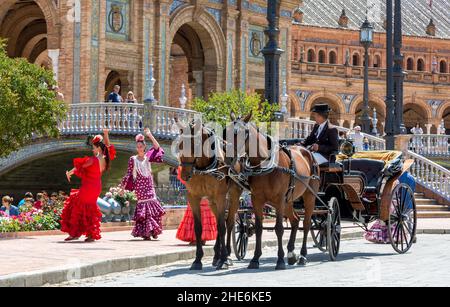 Ladies in traditional flamenco costumes dance at the Plaza de Espana, as their horse drawn carriage waits to take them to the annual Feria de Abril. Stock Photo