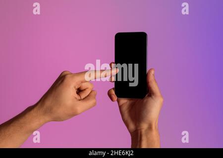 Unrecognizable millennial guy using smartphone with blank screen in neon light, offering mockup for mobile app Stock Photo