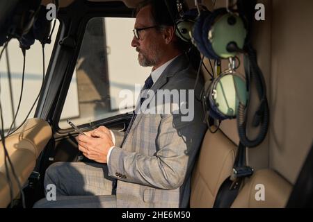 Serious thoughtful man with smartphone seated in helicopter cockpit Stock Photo
