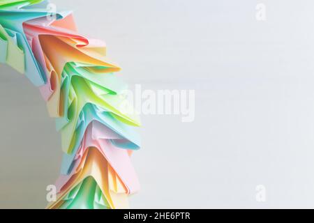 Origami ring fragment over white background, abstract parametric structure made of colorful paper sheets lays on a white wooden desk, top view