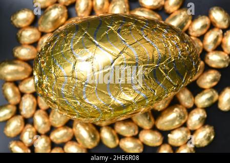 Pile or group of multi colored and different sizes of colourful foil wrapped chocolate easter eggs in gold and silver with a large gold milk chocolate Stock Photo