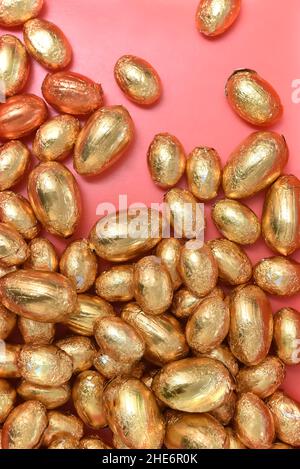 Large and small pile or group of gold, orange and bronze foil wrapped chocolate easter eggs, against a peach orange background. Stock Photo