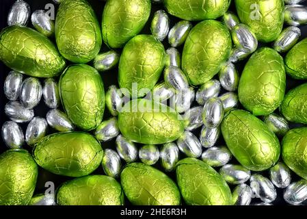 Large & small green, lime green and silver spring colours of foil wrapped chocolate easter eggs, against a black background. Stock Photo
