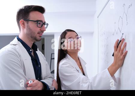 Two chemical students writing the chemical formulas on whiteboard. Stock Photo