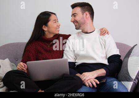 Young couple relaxing on a couch at home using laptop and smiling. Stock Photo