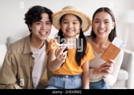 Smiling young girl in hat hold plane, selective focus. Millennial japanese parents happy and show passport and tickets Stock Photo