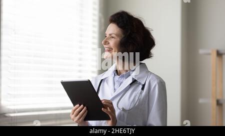 Dreamy happy old female doctor using digital tablet. Stock Photo