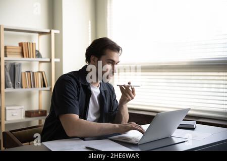 Focused young male employee recording audio, working on computer. Stock Photo