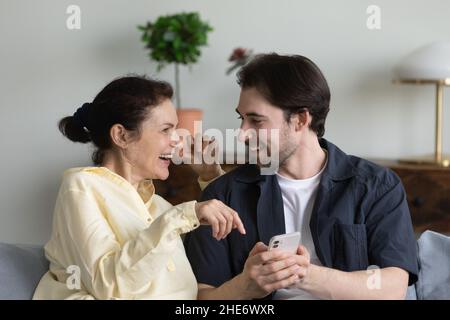 Happy young man using cellphone with mature mother. Stock Photo