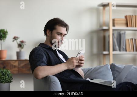Happy relaxed young man using cellphone at home. Stock Photo