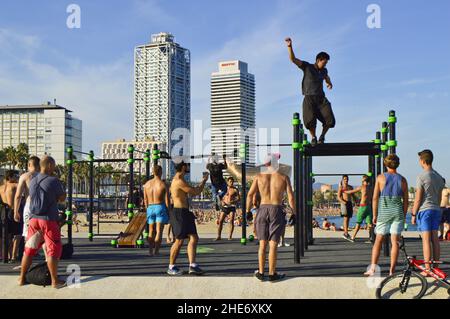 Men exercise on the beach of Port Olimpic with Torre Mapfre and Hotel Arts landmark skyscrapers in background, Barcelona Spain. Stock Photo