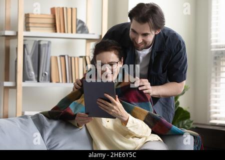 Happy old woman using tablet, spending time with caring son. Stock Photo