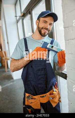 Cheerful man fixing window with silicone adhesive gun Stock Photo