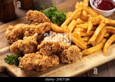 Crispy fried chicken tenders and french fries garnished with parsley on a wooden cutting board Stock Photo