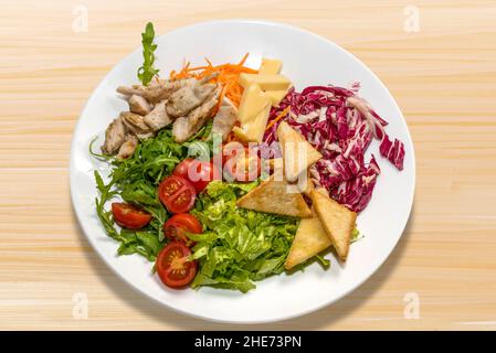 Caesar salad with chicken, cheese, tomato and croutons in white plate on wooden background Stock Photo