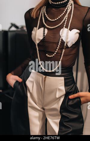 Cropped figure of fashion model woman wearing creative top with hearts, black and white pants with zipper and pearl beads. Fashion stylish female clot