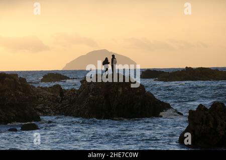 Dunure, Ayrshire, Scotland, UK Waves ,Firth of Clyde. Two people stood on a rock look at Ailsa Craig Stock Photo