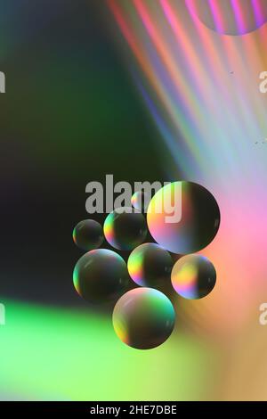 close-up of large and small oil droplets floating on a water surface and illuminated with colored light Stock Photo